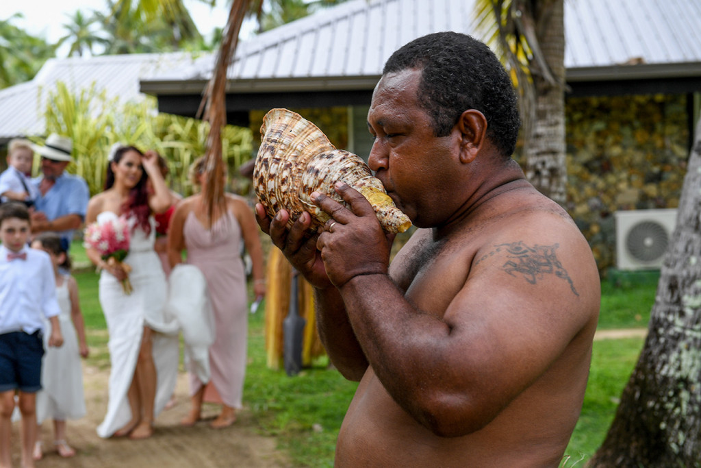A traditional Fiji warrior blows into a shell during the wedding ceremony
