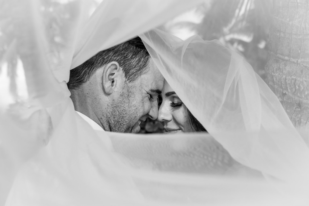 Under the veil: Monochrome image of the Bride and groom share an intimate moment wrapped in the bride's veil