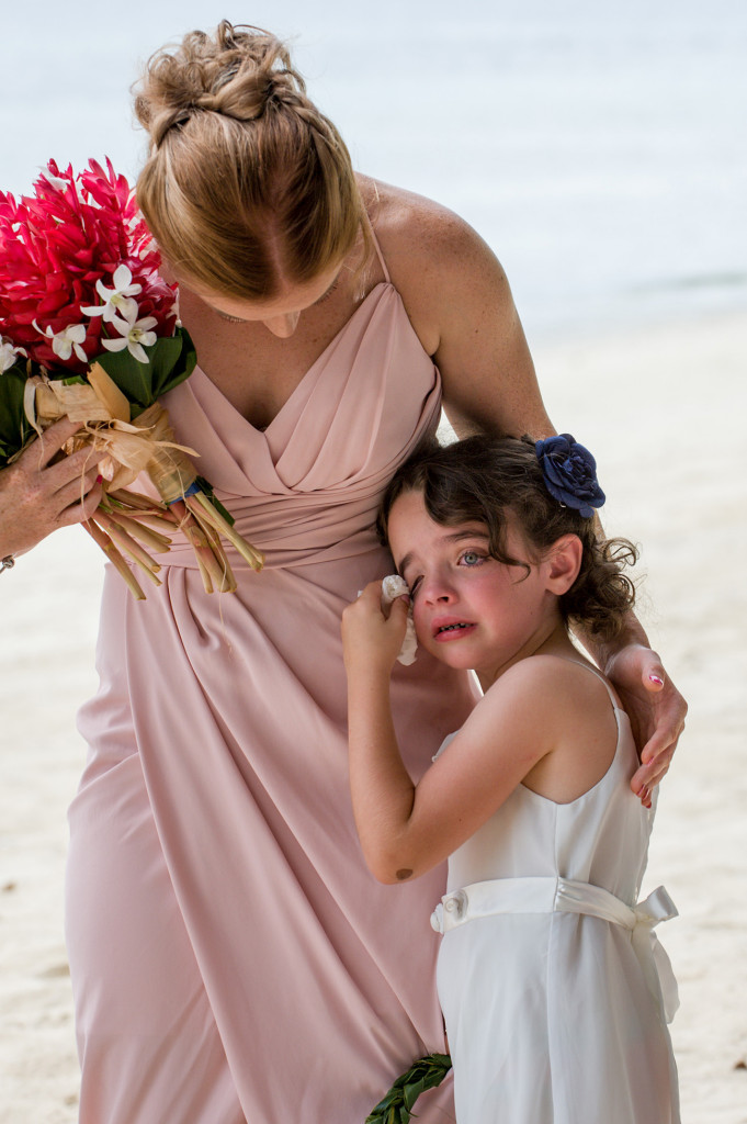 The flower girl wipes tears as she watches her parents marry