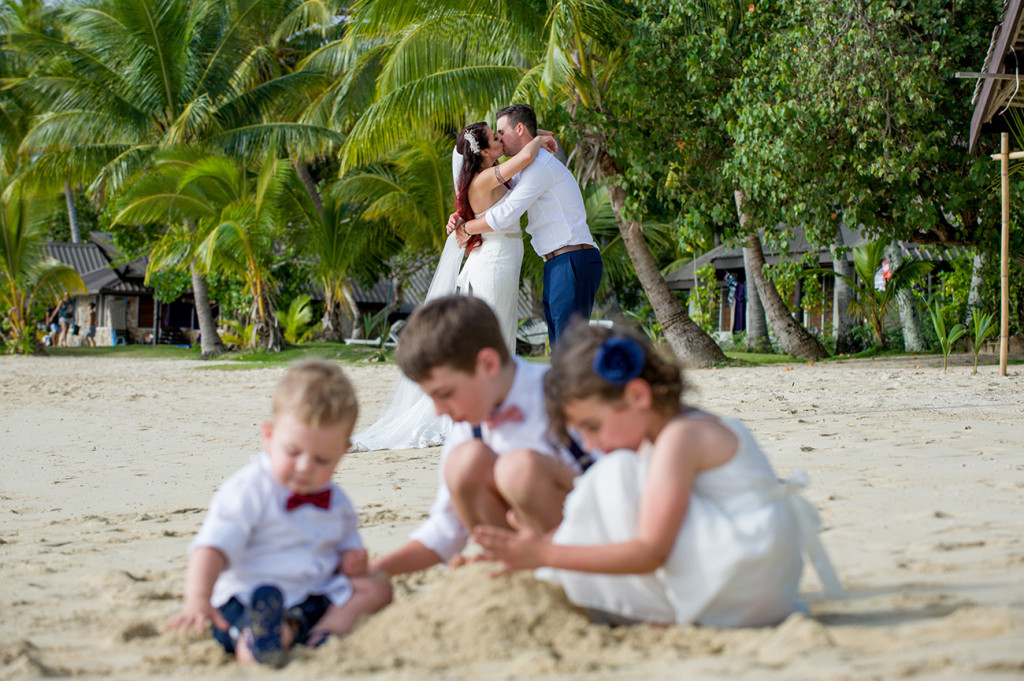 The children play in the foreground as the married couple kiss in the background