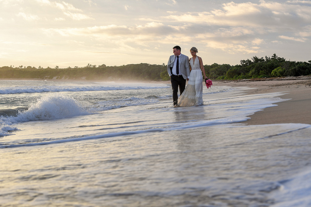 Newly wed bride and groom stroll hand in hand on the Fiji Coral Coast on their elopement