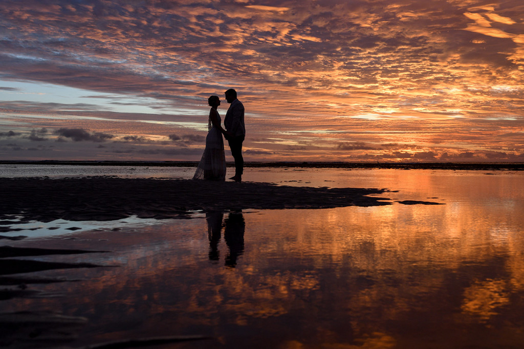 Silhouette of intimate bride and groom against fiery Fiji sunset