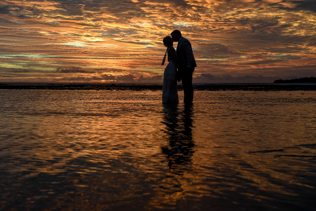 Silhouette of bride and groom kissing in the ocean against golden Fiji sunset