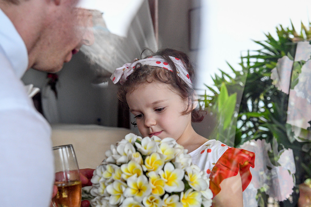 Cute flower girl in a polka dot head scarf admires the Frangipani flower bouquet