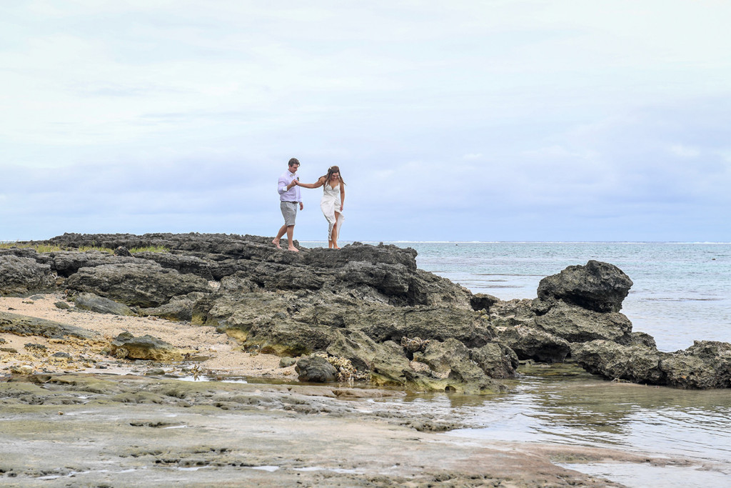 Bride and groom hold hands on coral rock at Maui Bay