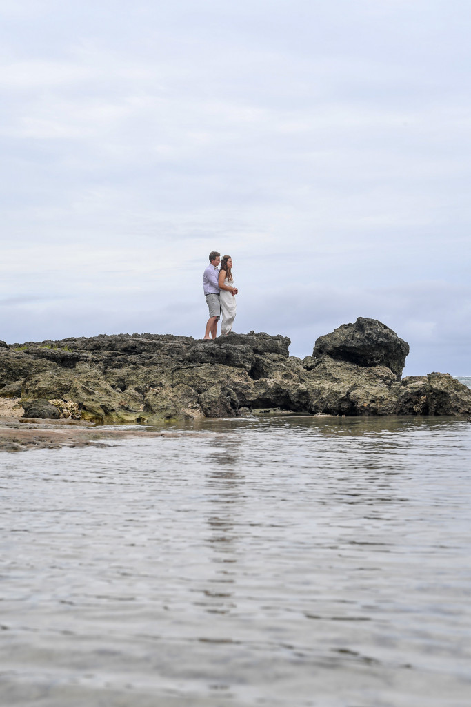 Bride and groom cuddle on a coral rock in Maui bay