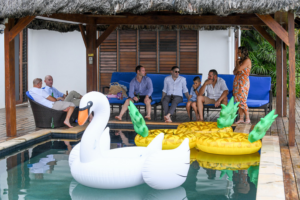 Men seat around the pool with giant swan and pineapple floaties