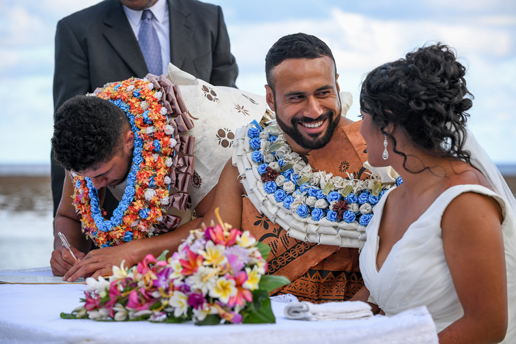 The groom smiles at his bride while his bestman signs the marriage certificate