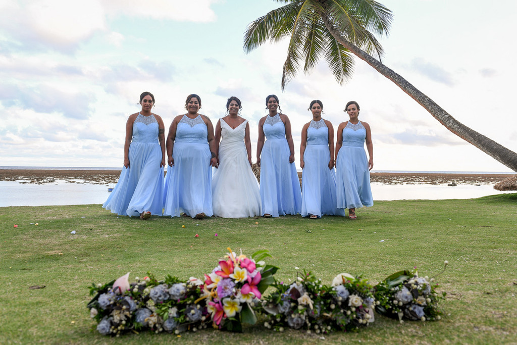 Bride and bridesmaids line up for a photoshoot against palm trees and sea