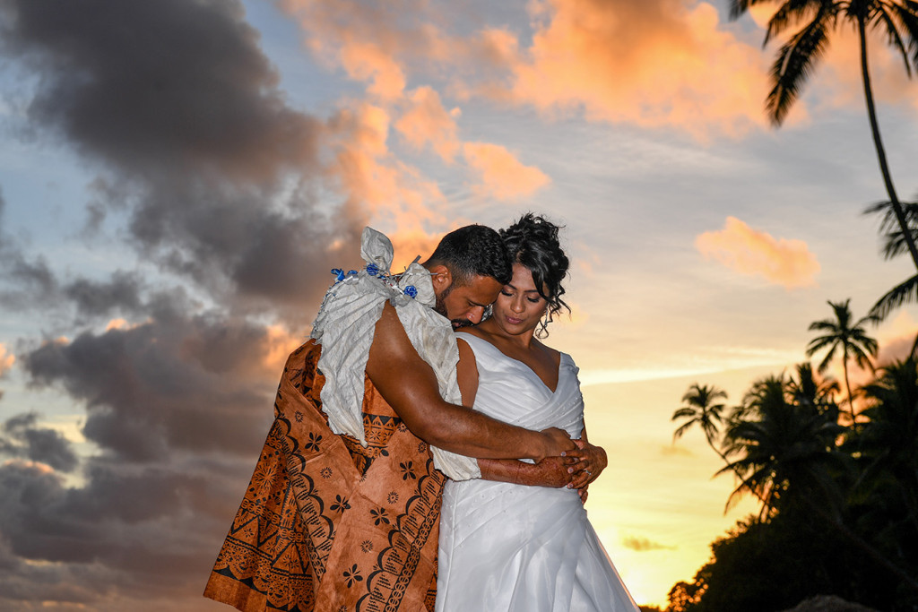 The groom delicately kisses his bride's shoulder in the golden Fiji sunset