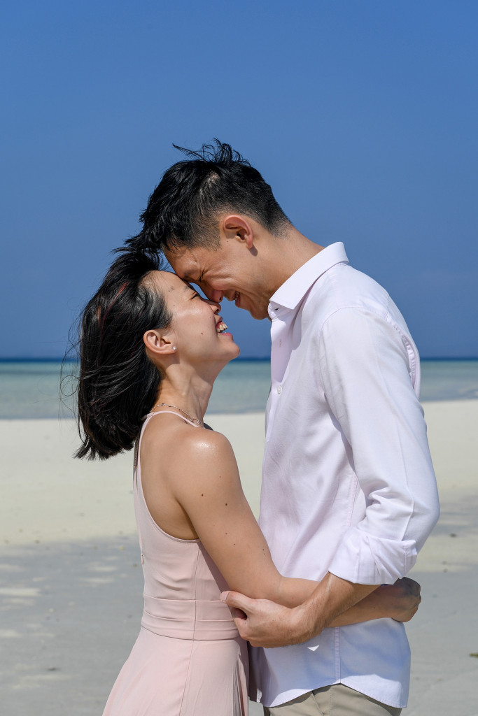 The couple laugh with each other while standing against deep blue skies