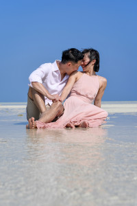 The groom playfully bites his bride's shoulder while seated in the shallow waters of the reef