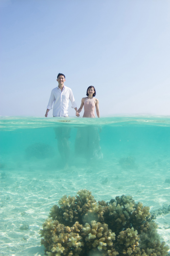 A mid-underwater shot of the couple walking towards a coral