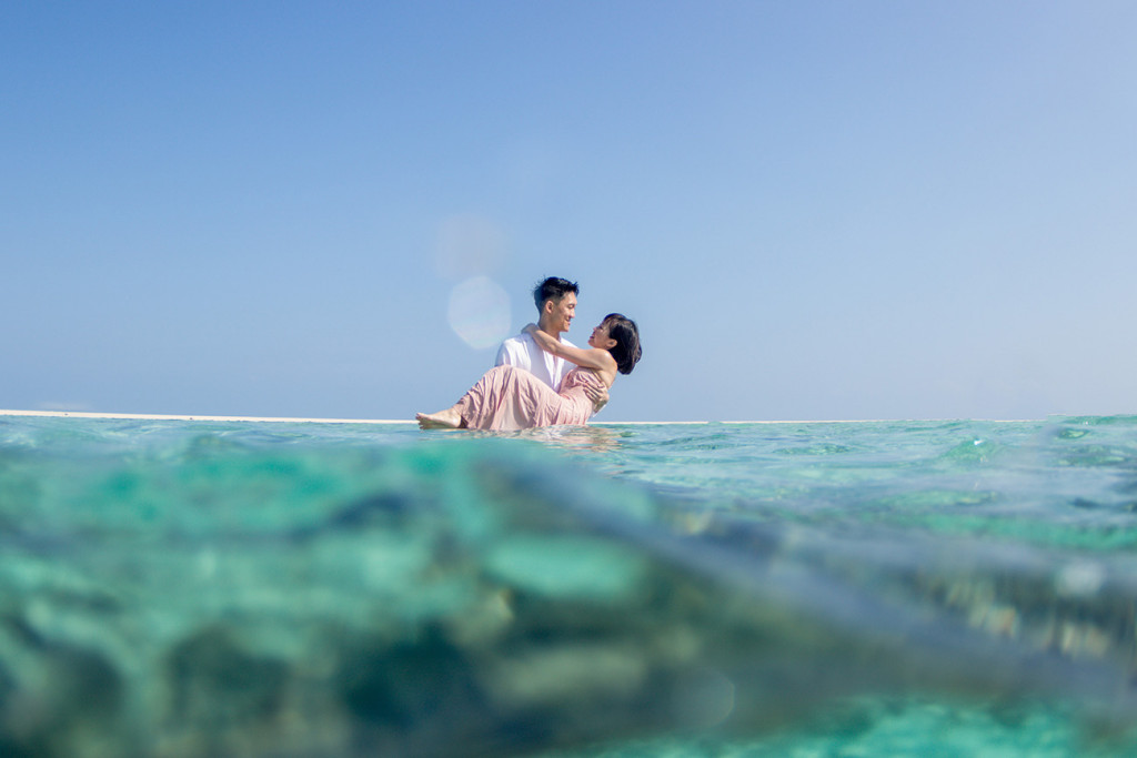 The groom suspends his bride above the surface of the ocean