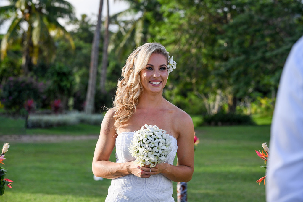 Bride smiles as she walks down the aisle holding her frangipani flower bouquet