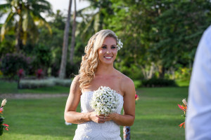 Bride smiles as she walks down the aisle holding her frangipani flower bouquet