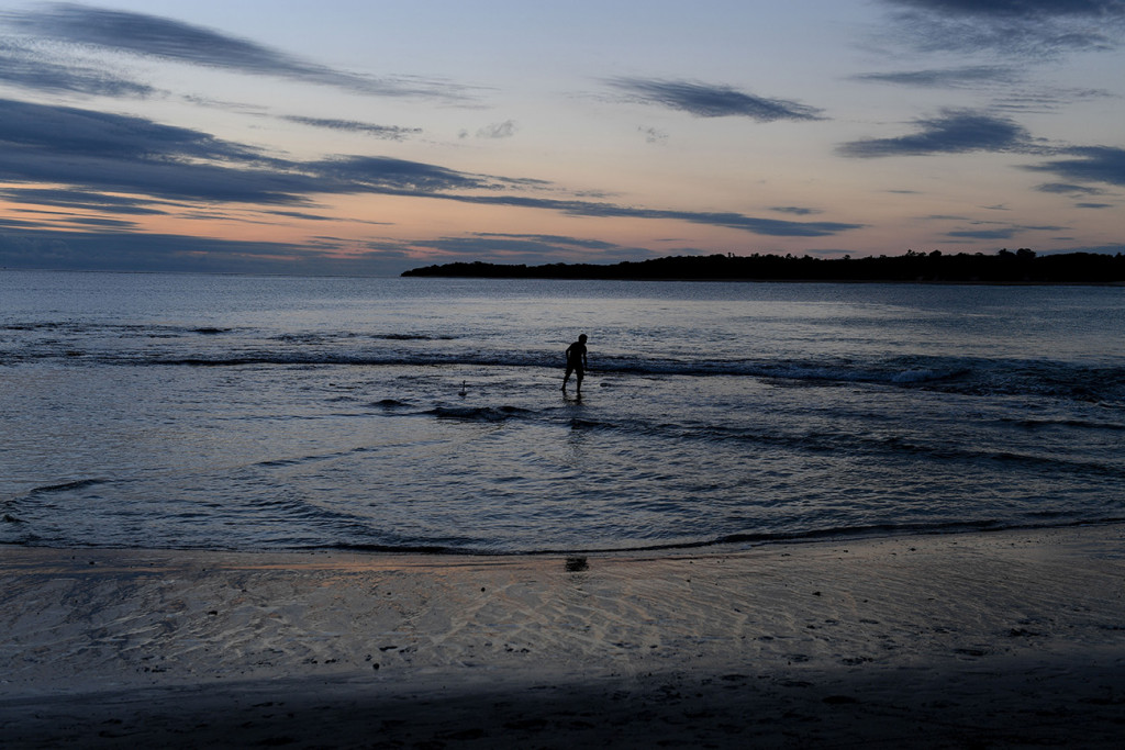 A lone boy plays in the ocean at dusk