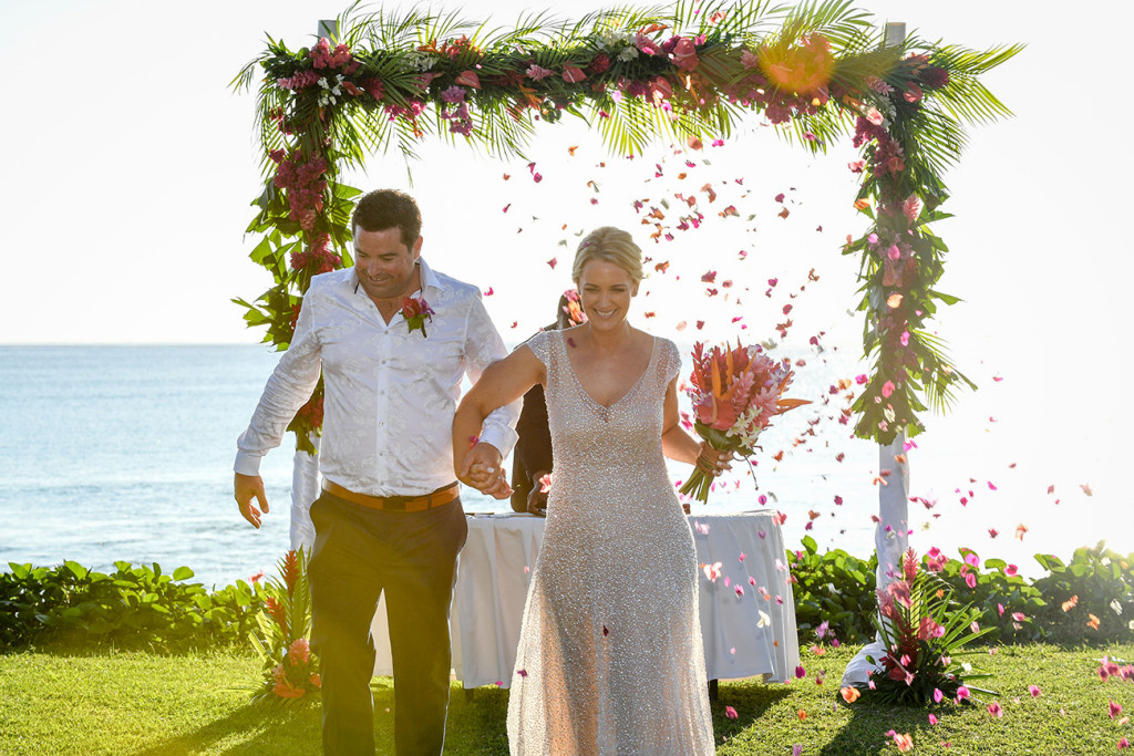 Flowers are strewn on the married couple as they walk from the altar at the beach