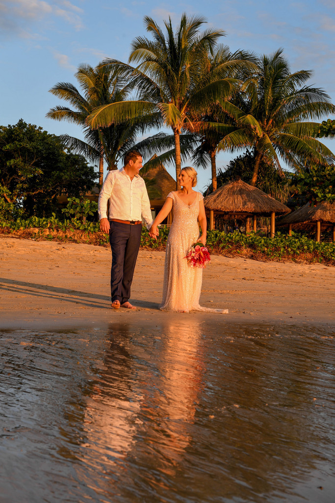 The orange sunset glows on the couple as they walk into the ocean