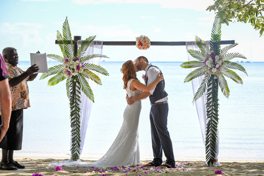 The bride and groom kiss while framed under the altar made of palm twigs at the Pacific Ocean