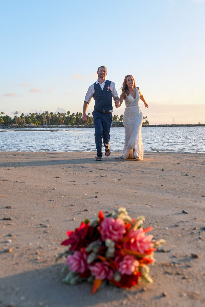 Bride and groom run towards the tropical flower bouquet