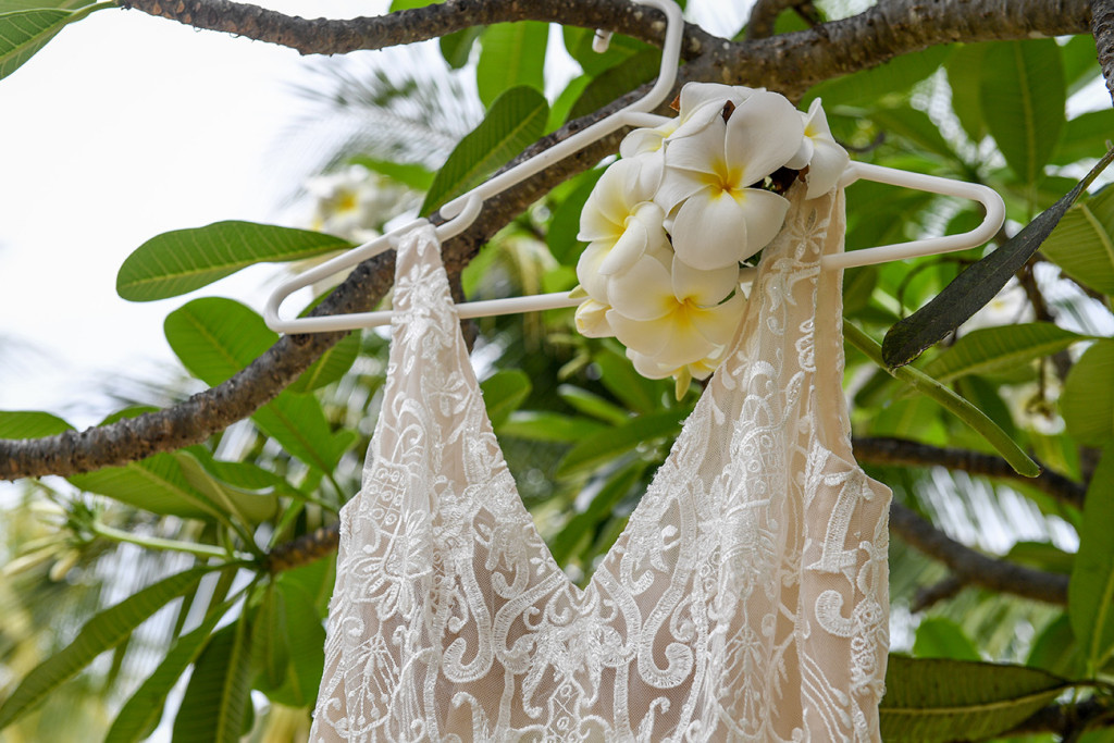 V shaped neckline of dress from Luv Bridal hanging beside a bouquet of tropical Frangipani flowers