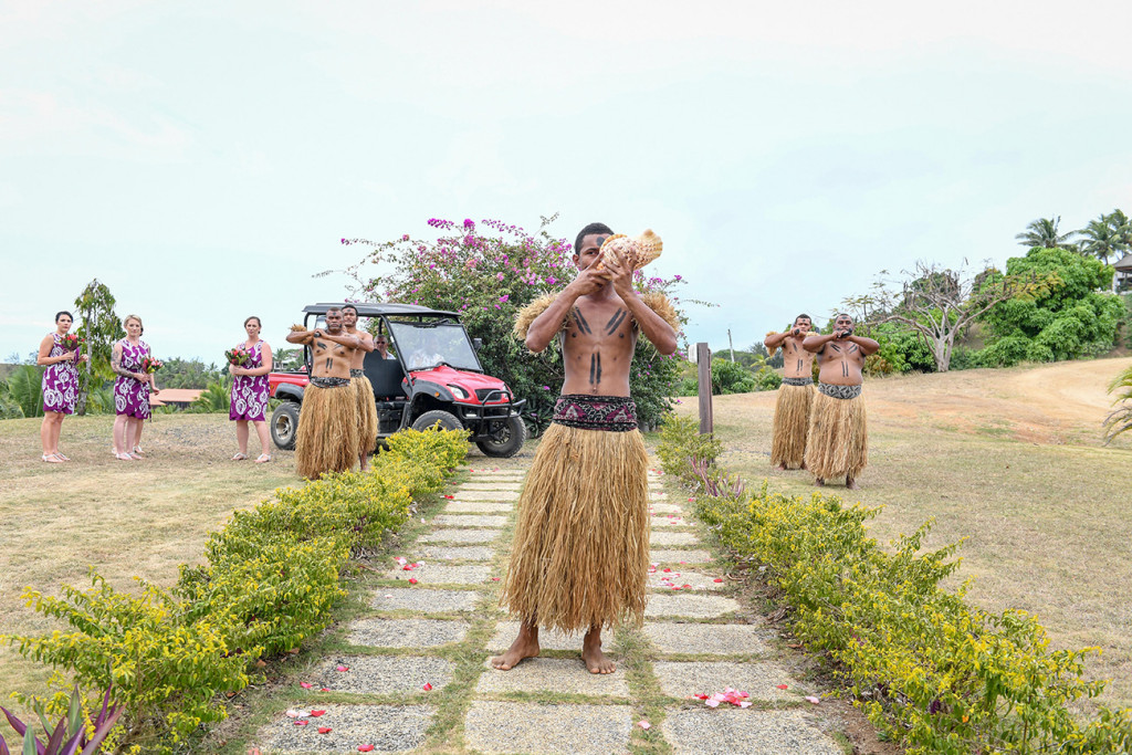 Traditional Fiji groomsmen blow a horn made from a seashell