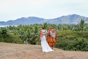 The newly married couple walks toward palm trees that litter the breathtaking Fiji landscape