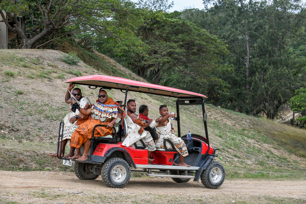 The groom and his groomsmen ride up in a red golf cart
