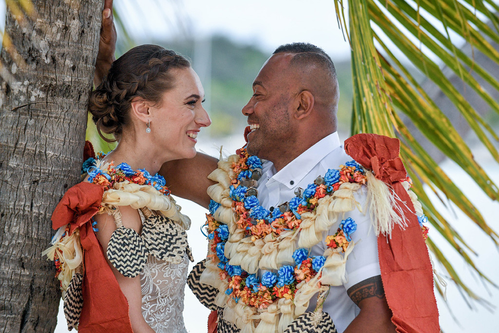 The bride and groom laugh with each other while under a palm tree