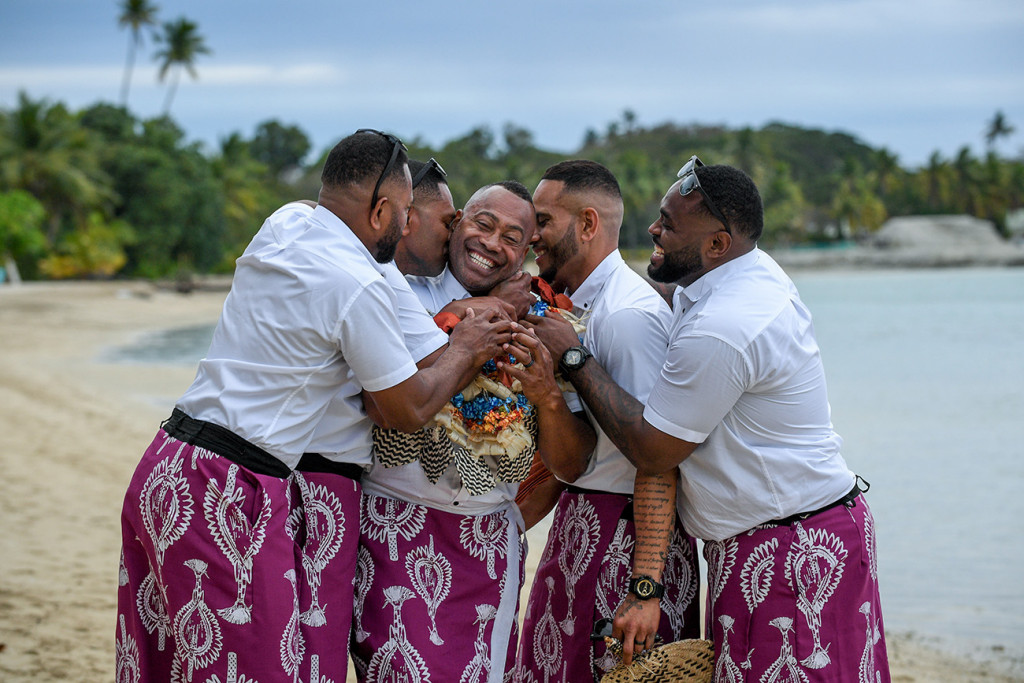 The groomsmen cheekily cuddle and kiss the groom at the shores of the Pacific