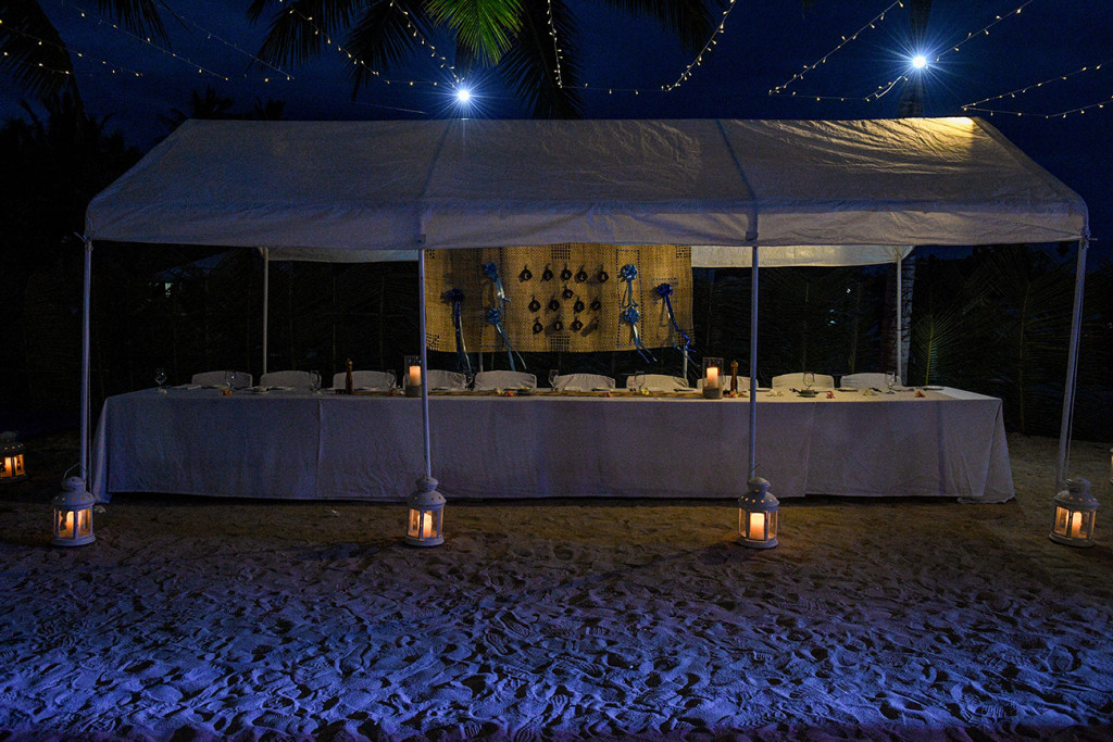 An intimate wedding reception setup on the beach under the stars with fairy lights and lanterns