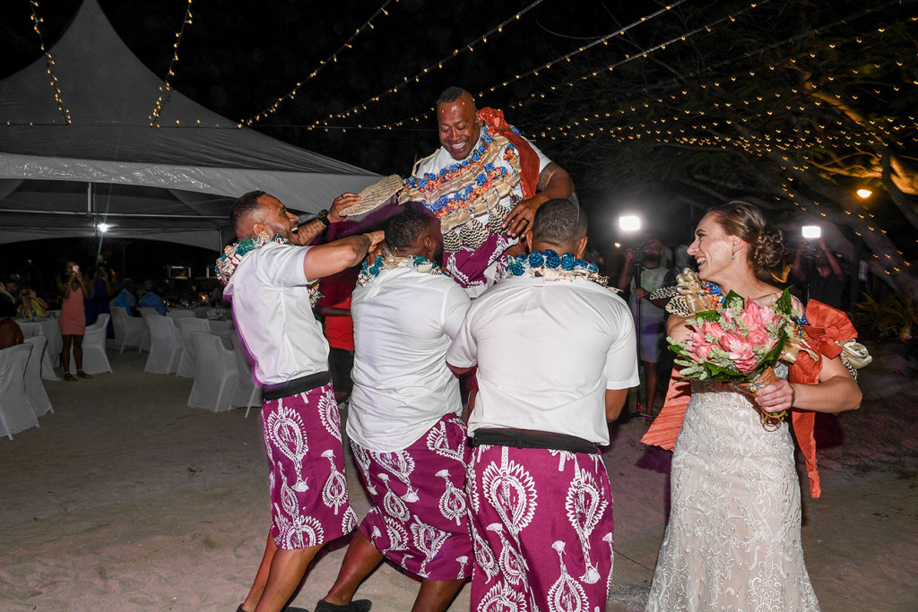 The groom laughs as the groomsmen lift him into the air against the fairy lights