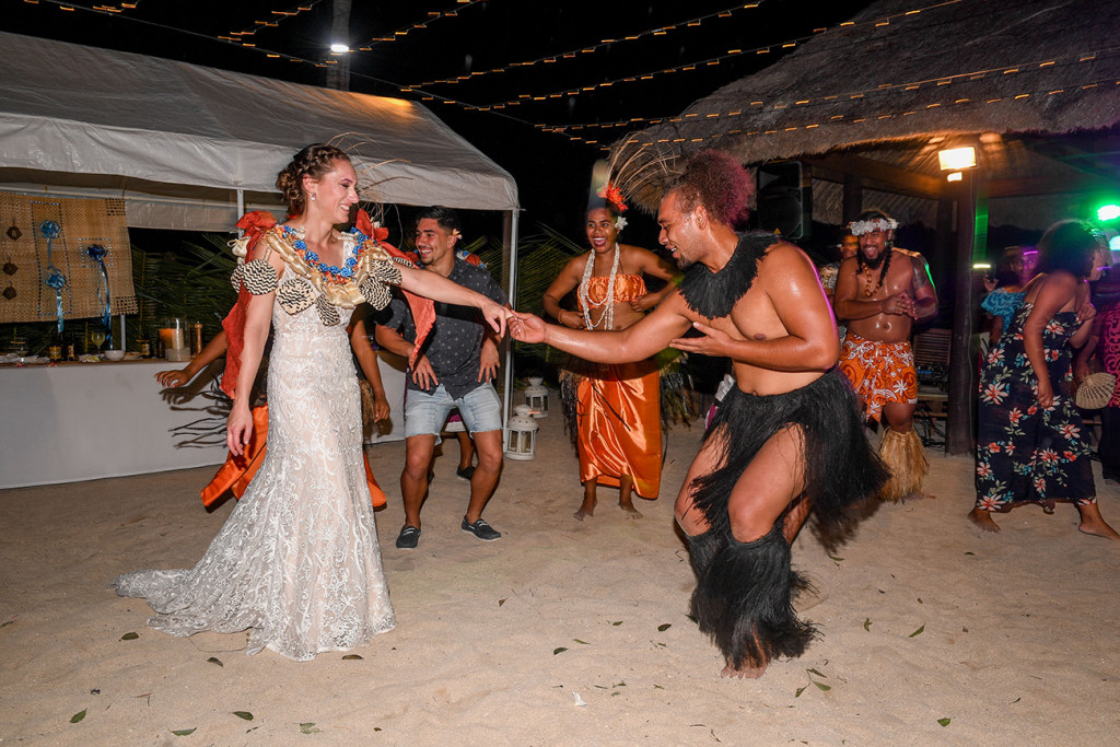 The bride dances with a Fiji performer on the beach at their wedding reception