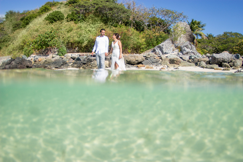 Bride and groom hold hands as they wade through turquoise waters at Castaway