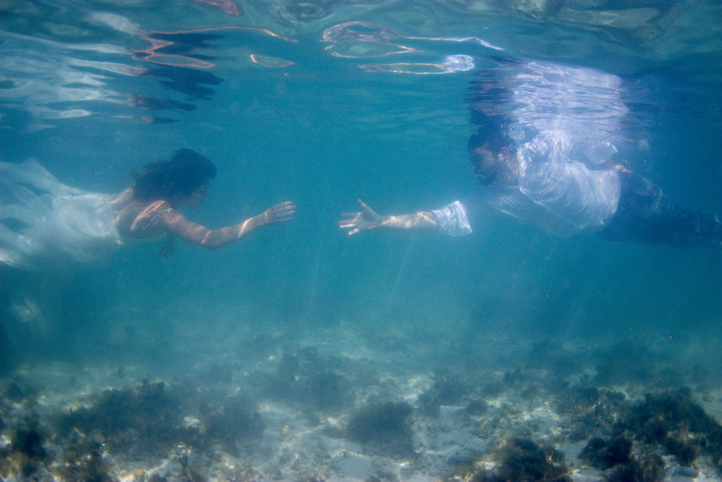 Bride and groom reach out to each other underwater