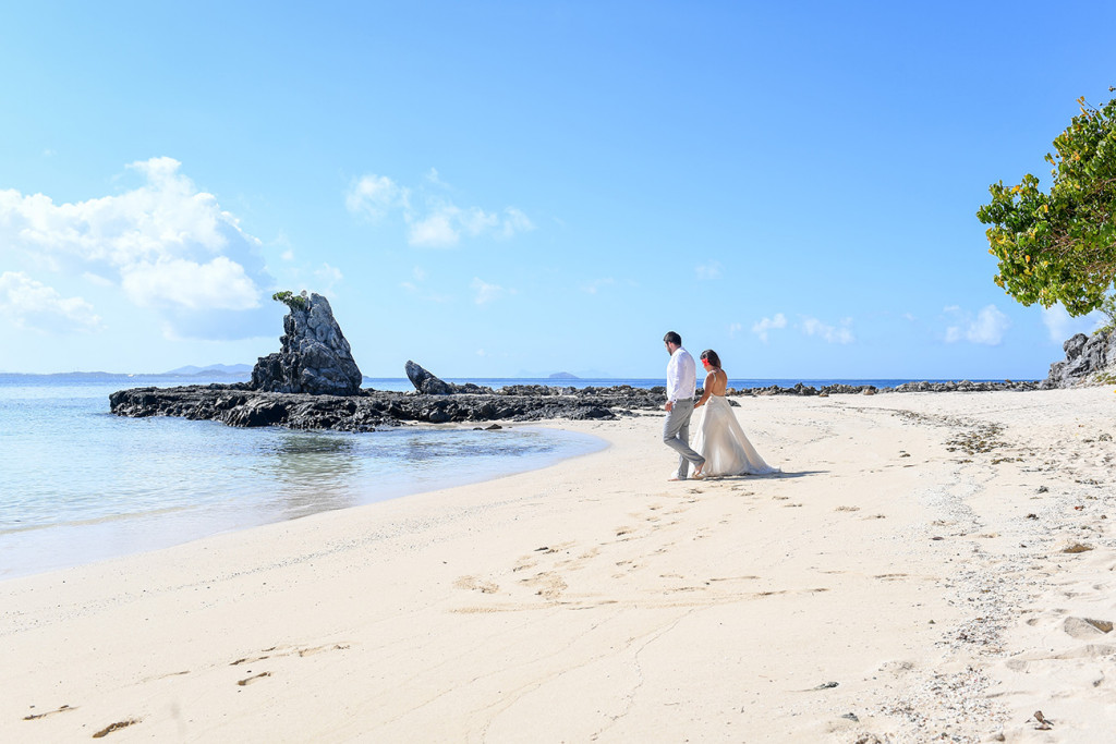 The stunning couple stroll towards the sea at Castaway Fiji reef on a sunny and bright day