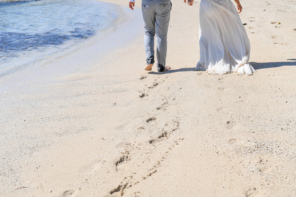 The couple leave footsteps in the sand as they walk towards the sea at their honeymoon