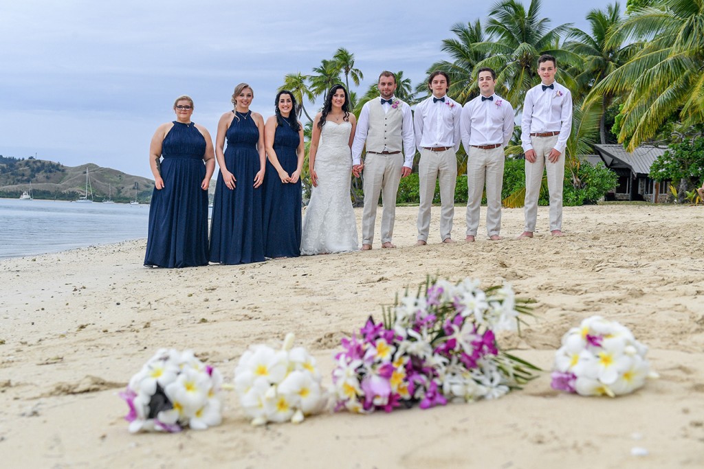 The bridal party poses in front of their flower bouquets