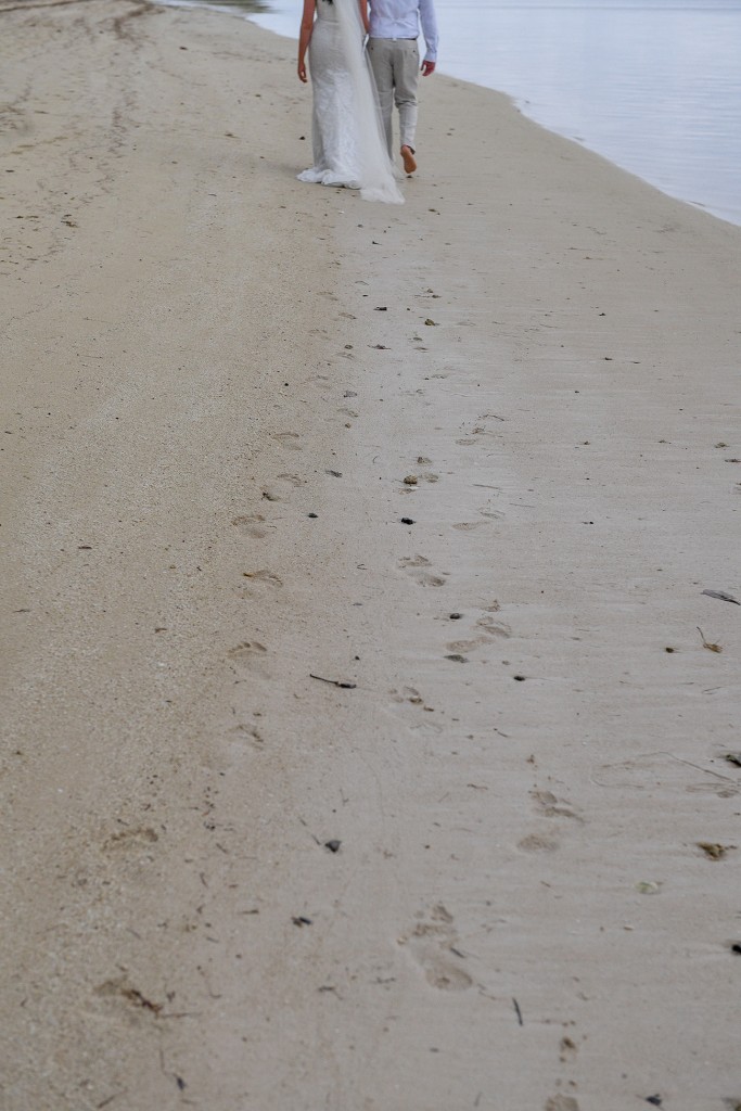 The newly weds leave fresh footprints in the sand as they stroll on the beach