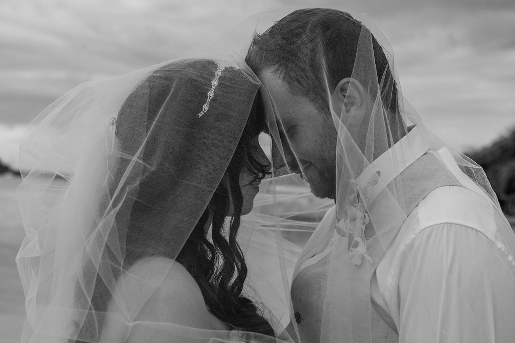 A monochrome photograph of the newly weds being intimate under the veil
