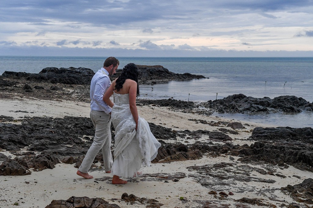 The newly weds walk on rocky beach to pose for their photos