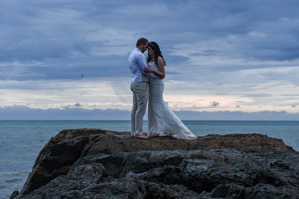 The newly weds share an intimate moment atop a rock against a glum sunset