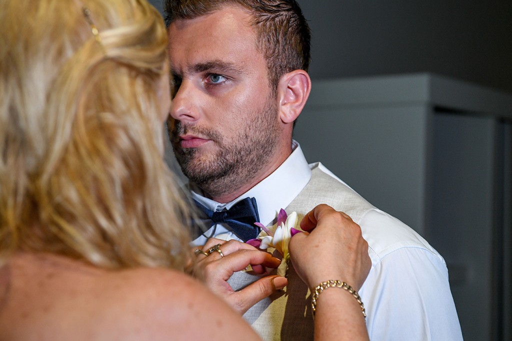A bridesmaid helps the groom pin the flower boutonniere on the groom