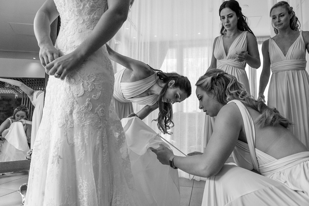 Bridesmaids help the bride into her dress