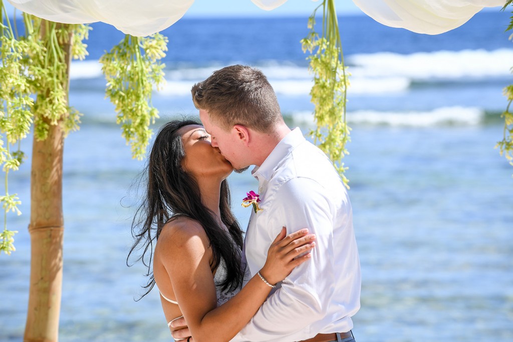The married couple kiss under the bamboo altar at the Pacific Ocean
