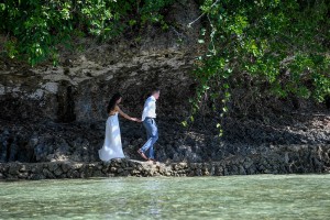 The newly married couple walks over rocks by the azure Pacific Ocean