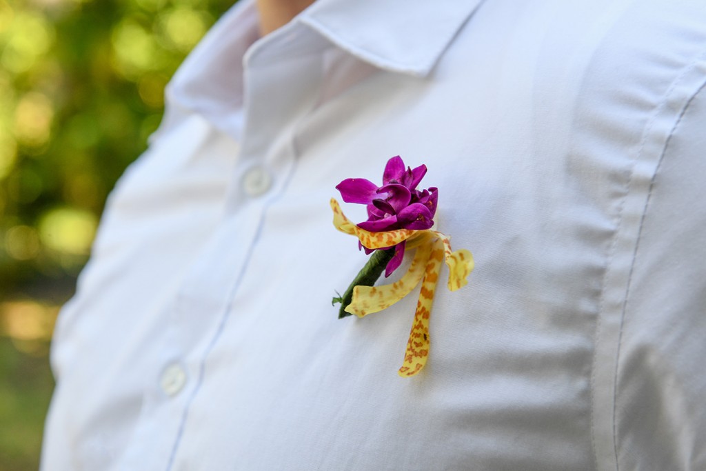 A closeup of the pink fresh flower boutonniere on the grooms shirt