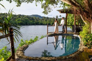 The groom and bride stare into the sunset standing next to a tiny infinity pool
