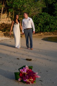 The groom makes his bride laugh as they stroll on the beach